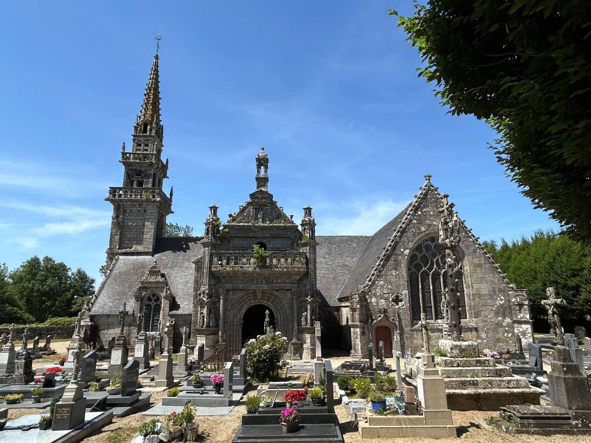 Stone Gothic church with spires and a surrounding graveyard under a blue sky.